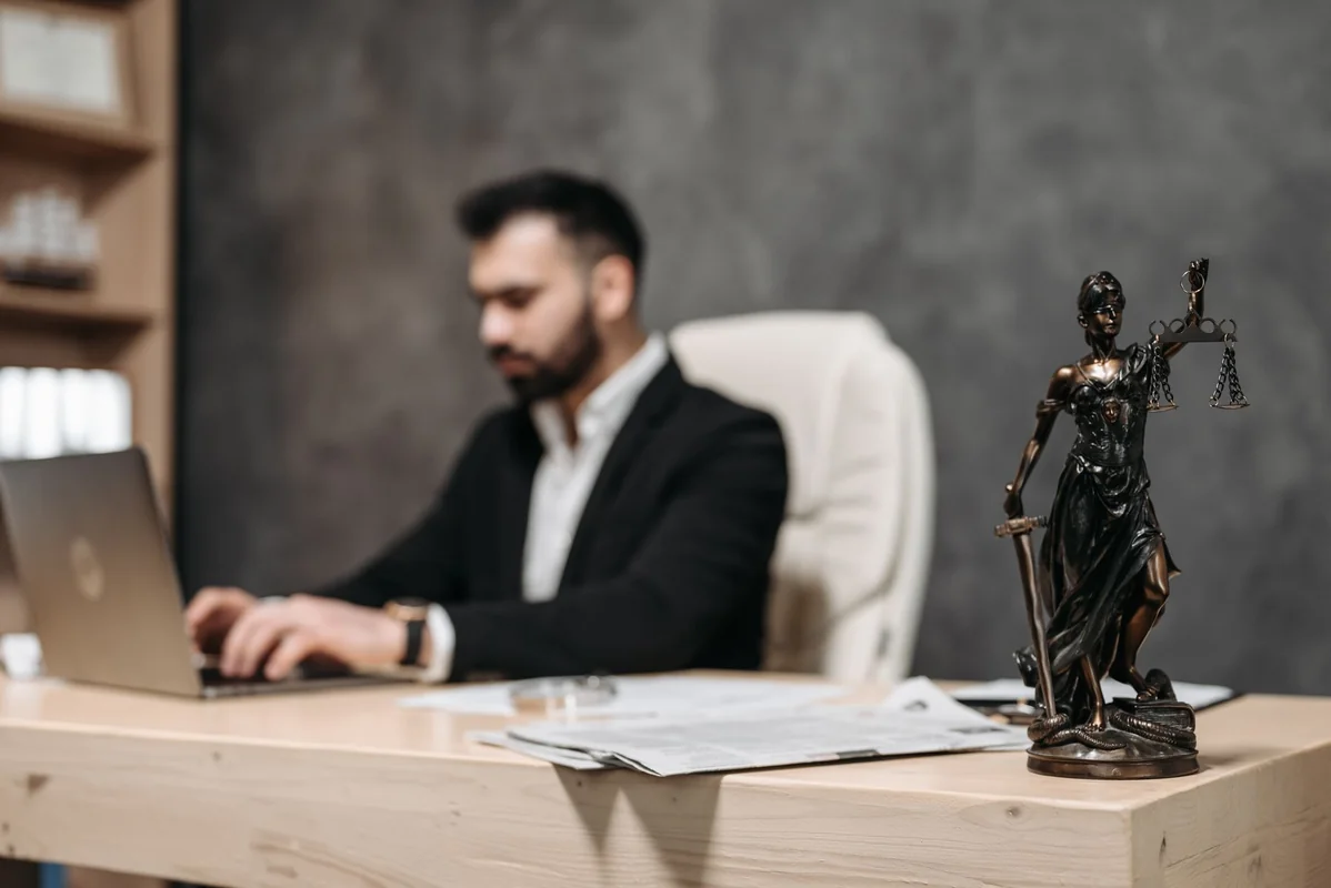 A businessman working on a laptop in an office with a Lady Justice statue in foc